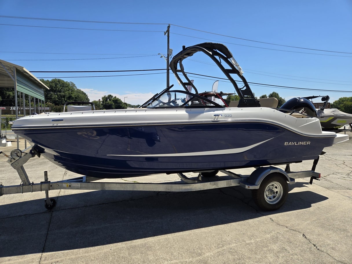 A navy Bayliner D20 bowrider with a wake tower on a trailer in a paved lot.