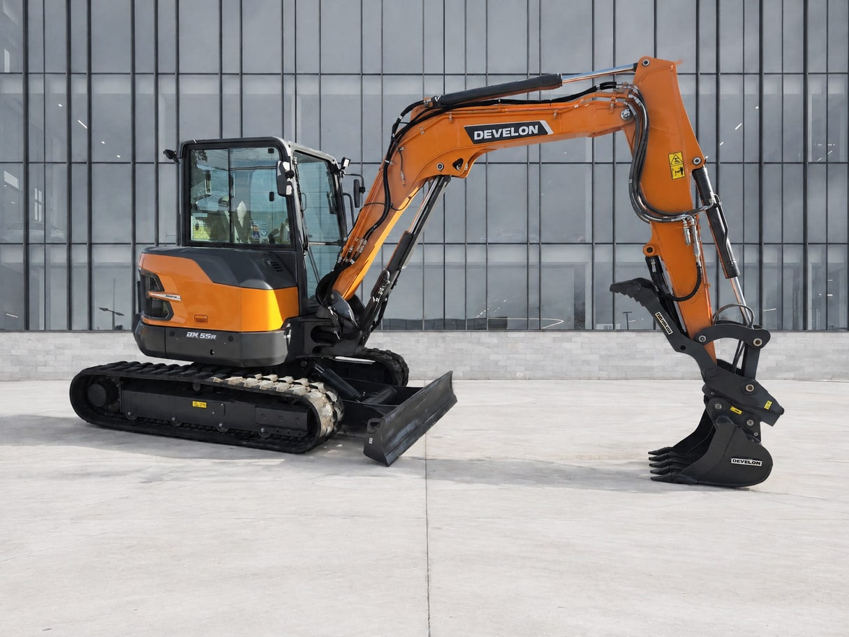 The same Develon excavator on a pale concrete forecourt in front of a glass building.
