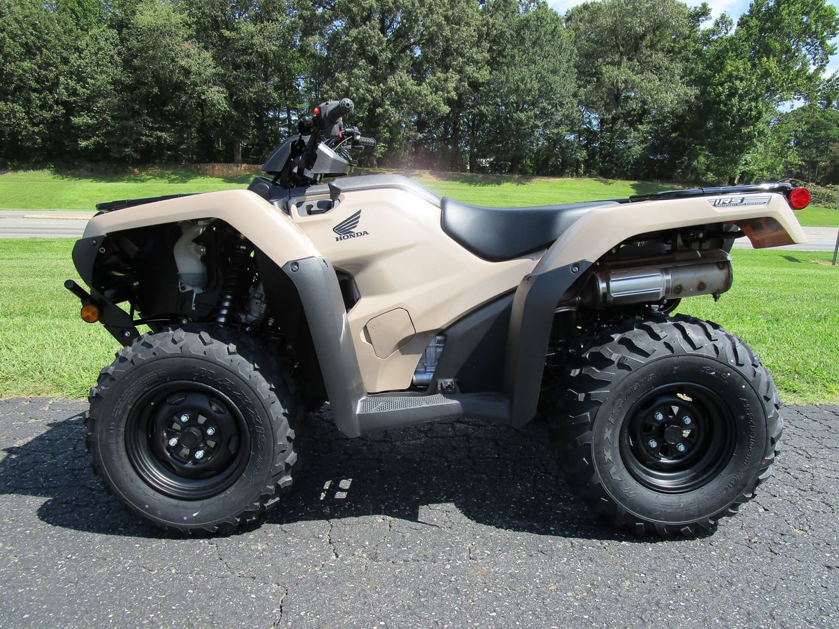 A tan Honda FourTrax Rancher ATV on asphalt in front of a lawn and trees.