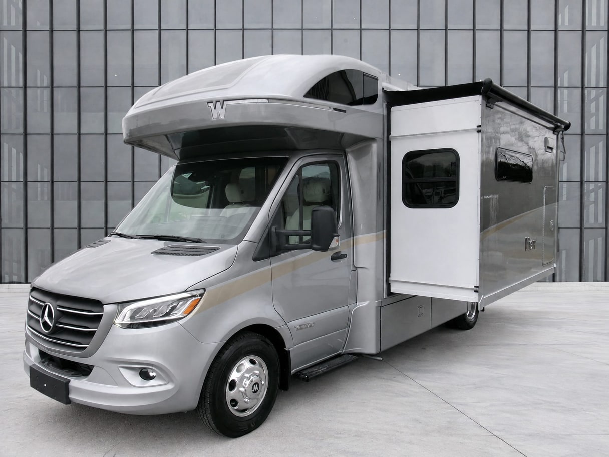 The same Winnebago View motorhome on a concrete forecourt in front of a glass building.