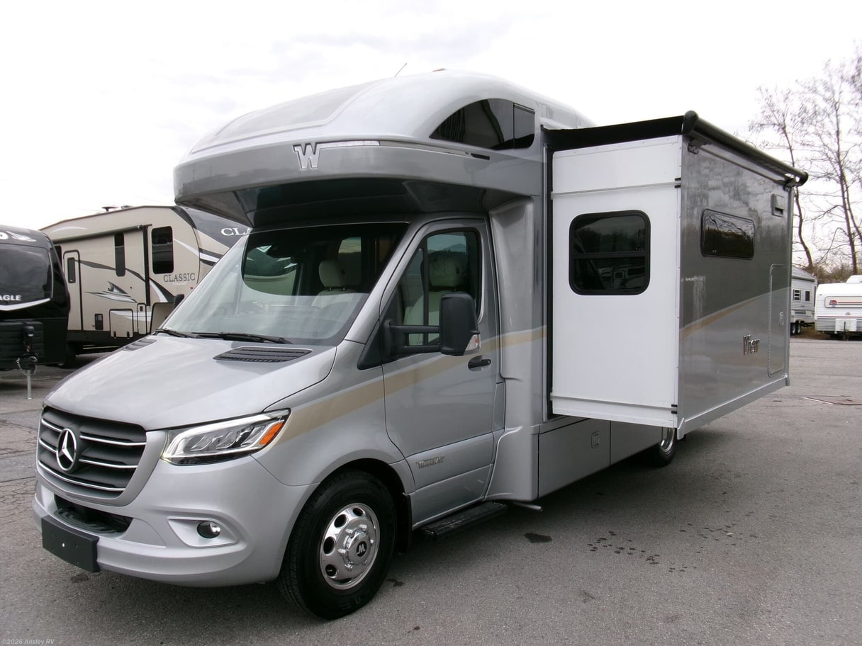A silver Winnebago View 24T Class C motorhome on a paved lot beside other RVs.