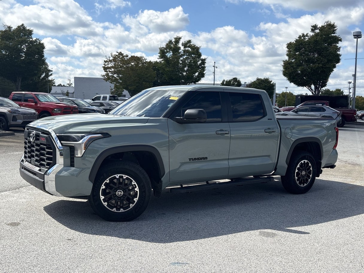 A grey 2024 Toyota Tundra crew cab in a dealership lot under a cloudy sky.
