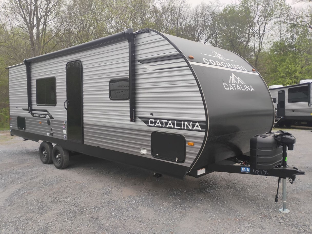 A 2026 Coachmen Catalina travel trailer on a gravel lot with trees behind it.